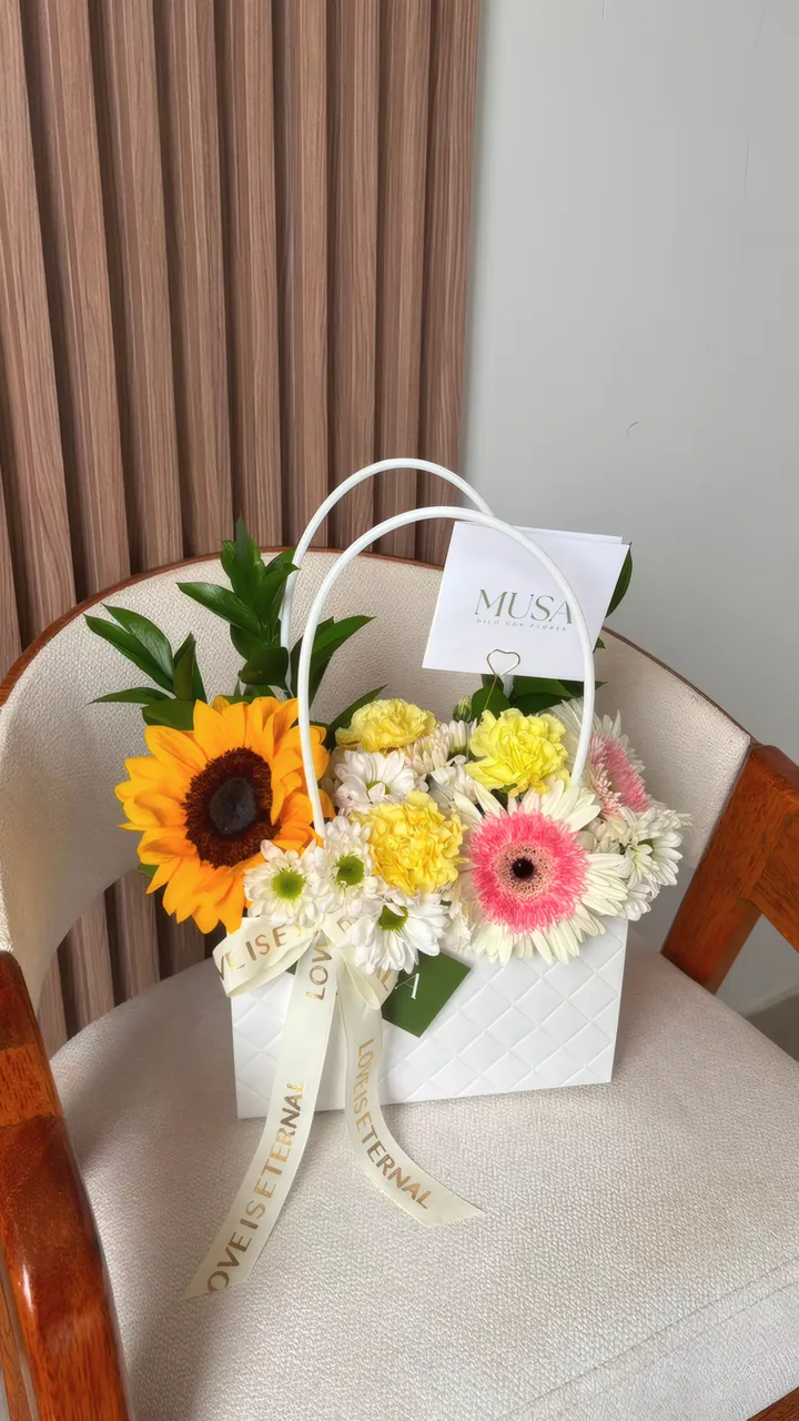 Cartera floral Escencia: girasol, gerbera rosada y margaritas en cartera blanca