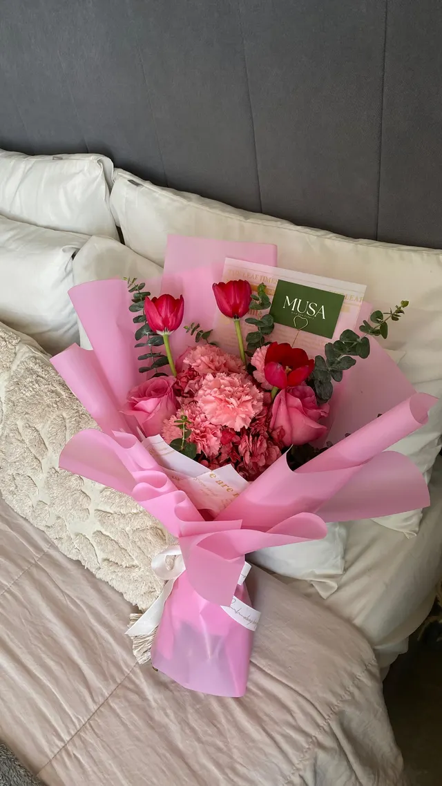 Ramo de rosas y claveles rosados sobre una cama